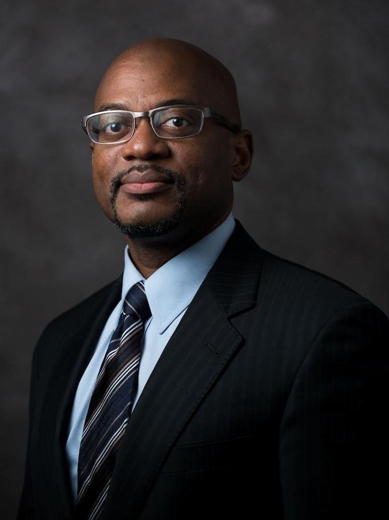 A dark skinned man in a suit looking at the camera